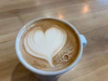 Tahta bir masada, beyaz bir fincanda sıcak kahve.