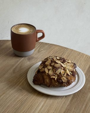 Bir fincan kahvenin dikey görüntüsü ve ahşap bir masada kruvasan.