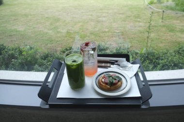 Bir fincan kahve, bir fincan kruvasan ve bir kafenin arka planındaki ahşap masada yeşil bir bitki..