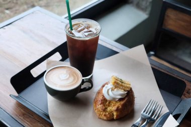 Kahve ve kruvasan. Kafedeki ahşap masada buz ve süt var.