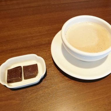 Bir fincan sade kahve ve siyah çay tabağı ve ahşap arka planda bir kaşık ile beyaz çikolata.