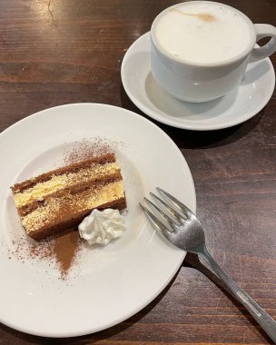 Bir fincan kahve ve çatallı lezzetli bir kekin dikey çekimi.