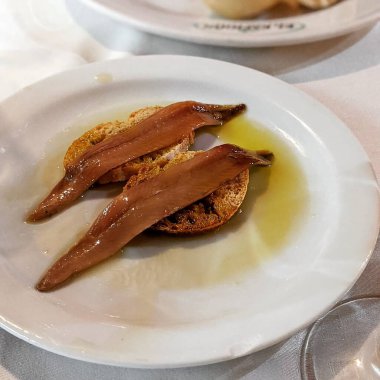 İki lezzetli tütsülenmiş somon diliminin yakın plan fotoğrafı beyaz bir tabakta zeytinyağlı bir masada.