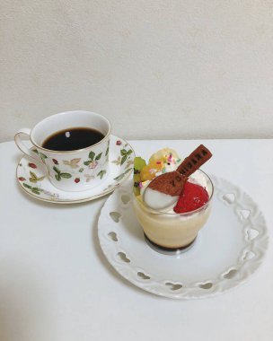 Krem şanti ve kahve fincanı beyaz bir masada duran lezzetli bir pastanın dikey çekimi.