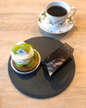 Bir fincan kahve, lezzetli bir pasta ve tahta bir masanın üstünde bir parça kek..