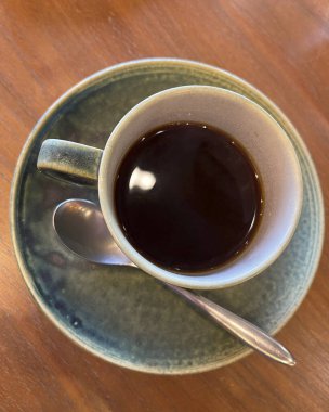 Tahta bir masada kaşık ile bir fincan kahve.