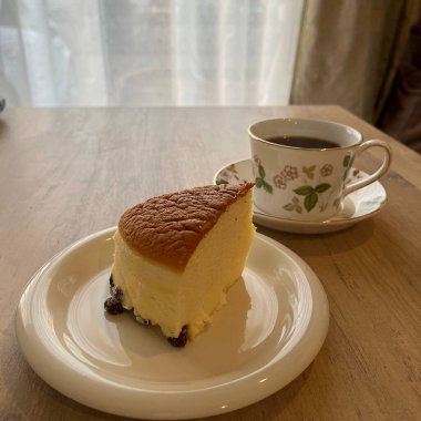 Tahta bir masanın üzerinde bir fincan kahveyle bir parça kek.