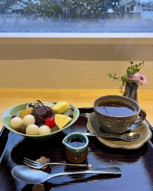 Bir bardak sütlü çay ve ahşap bir masada çaydanlık.