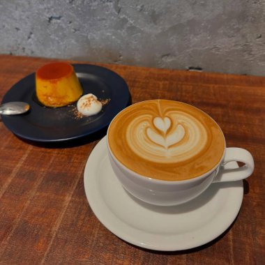 Beyaz fincanlı bir fincan sıcak kahve ve ahşap bir masanın üzerinde bir parça kek.