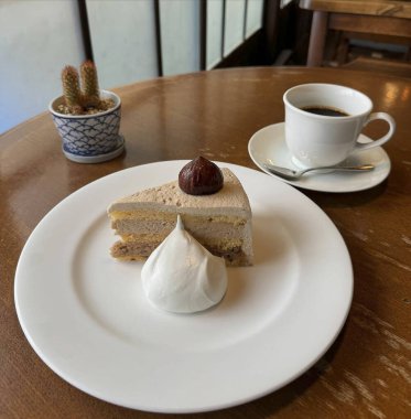 Bir fincan kahve ve bir dilim kek. Masadaki beyaz tabakta.