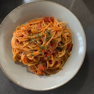 Domates soslu spagetti ve beyaz tabakta fesleğen.