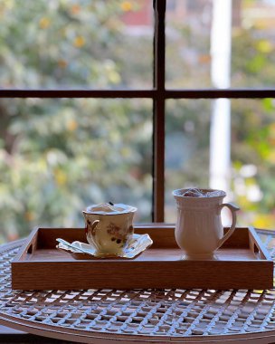 Beyaz tabakla bir fincan kahve ve tahta bir masada bir bardak süt.