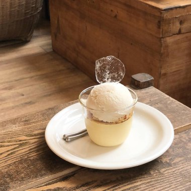 Tahta arka planda bir fincan kahve, kremalı bir bardak, bir kaşık, bir parça dondurma.