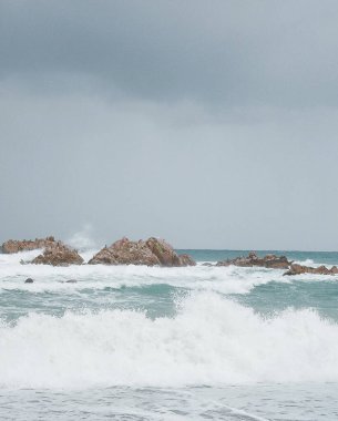 Dalgalar kayalara ve köpüğe çarpıyor.