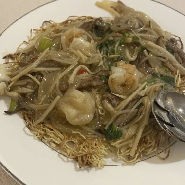 Beyaz tabakta deniz ürünleri ve sebzeli erişte.