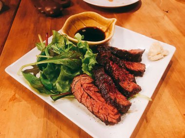 Tahta bir masada salata yaprakları ve otlarla nefis bir bifteğin yüksek açılı görüntüsü.
