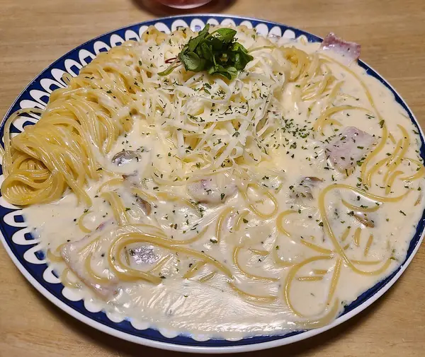 Beyaz tabakta makarna, krema ve pastırma ile ahşap bir masada.