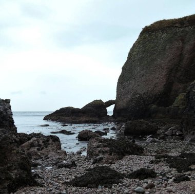 Önplanda bulutlu bir gökyüzü arka planıyla denizde kayanın dikey görüntüsü.