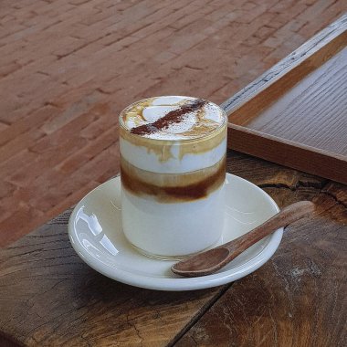 Kremalı ve kaşıklı bir bardak kahvenin dikey çekimi.