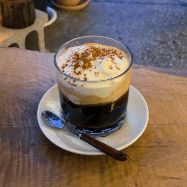 Tarçın çubuklu bir fincan sıcak kahve ve ahşap masada beyaz bir köpük.