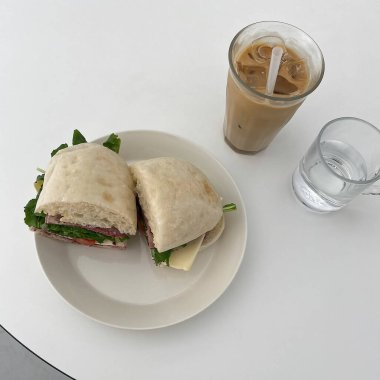 Masanın üzerinde bir fincan kahve ve bir sandviç.