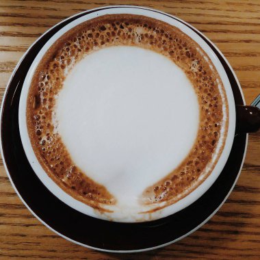 Ahşap zemin üzerinde köpük ve süt olan bir bardak kapuçino.