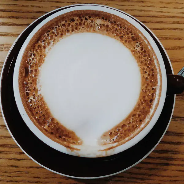 Ahşap zemin üzerinde köpük ve süt olan bir bardak kapuçino.