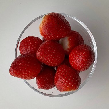 Beyaz arka planda cam bir kasede taze çilekler..