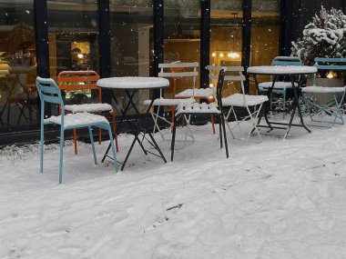 Sokakta karla kaplı boş masalar ve banklar.