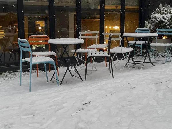 Sokakta karla kaplı boş masalar ve banklar.