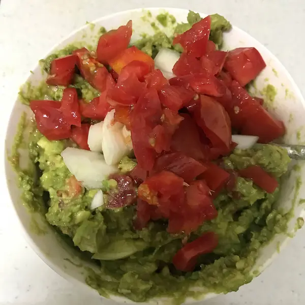 Tortilla cipsi, avokado, domates ve spatula ile bir kase guacamole..