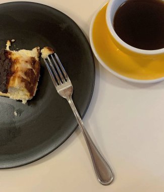 Bir parça kek, siyah bir tabak ve bir fincan kahveyle yakın çekim.