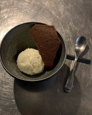 Dikey olarak bir kaşık ve siyah tabakta bir kase çikolatalı leziz dondurma.