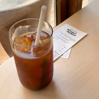 Bir bardak soğuk içecek, buz küpleri ve ahşap bir masada saman.