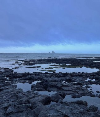 Akşamları okyanusta bulutlu bir havada kayalık sahilin dikey görüntüsü.