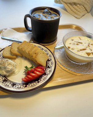 Bir fincan kahve, beyaz bir tabak krema ve beyaz bir tabak.