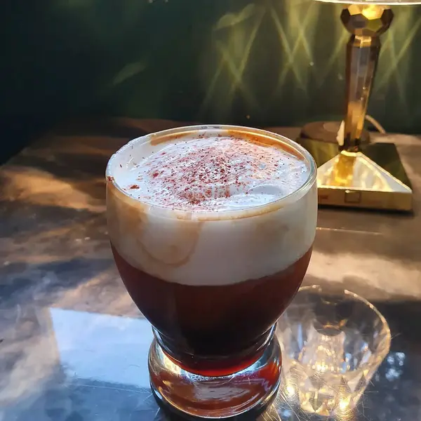 Bir bardak buzlu kahve. Ahşap bir masanın üstünde. Siyah bir arka planı var.