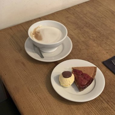 Bir fincan kahve, bir parça kek ve masanın üstünde bir tabak.