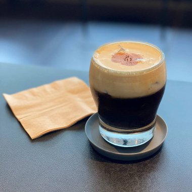 Bir bardak soğuk buzlu kahvenin yakın çekimi. Masanın üzerinde bir kaşık ve beyaz köpük var.