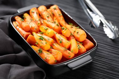 Kurutulmuş bal kaplı havuç kekik ile siyah ahşap bir masada seramik formda. Karamelli havuç. A vitamini bakımından zengin sağlıklı bir havuç tabağı..