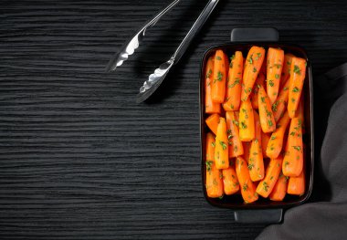 Koyu ahşap bir masada seramik formda kekik şeklinde ballı bebek havuçları, metin için kopyalama alanı. Sağlıklı yaz sebzeleri.