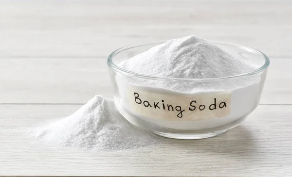 stock image baking soda in a clear glass bowl on a light wooden table. Glass bowl of sodium bicarbonate on a white wooden table.
