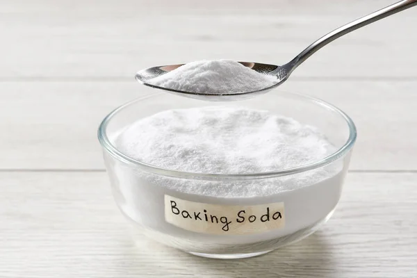 stock image bowl with sodium bicarbonate on a whitet wooden table, plate with baking soda on wooden table.