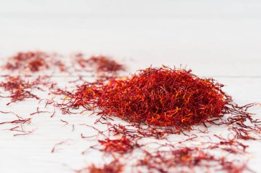 Beyaz ahşap bir masanın üzerinde damga safranı, seçici bir odak noktası. Parlak kırmızı safran iplik, crocus sativus 'tan türetilmiş baharat