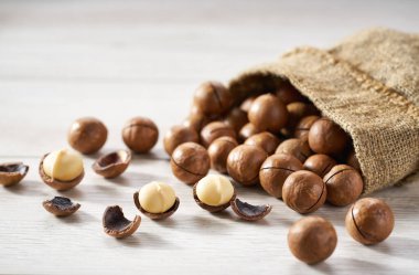 Beyaz ahşap bir masada çuval içinde Macadamia fındıkları..