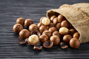 Çuval bezi içinde siyah tahta masada Macadamia fındıkları..