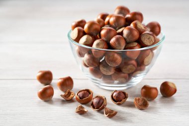 hazelnut in a clear glass bowl and scattered on a white kitchen table, selective focus.