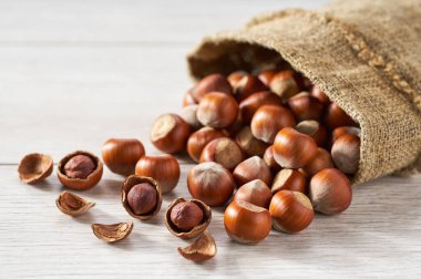 hazelnut nuts in burlap sack on a white wooden table.