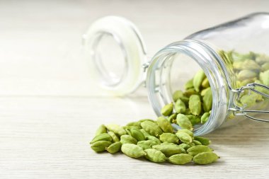 cardamom pods spill out of a glass storage jar on a  white wooden kitchen table, selective focus.