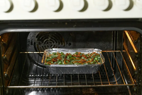 roasted green bean casserole with crispy fried shallots and cream sauce  in a disposable square aluminium foil baking dish in the oven, selective focus.